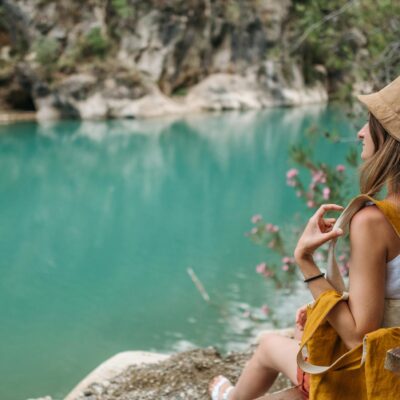 A woman sits on a lakeshore bench, enjoying serene turquoise waters and lush nature.