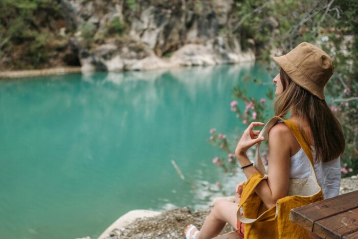 A woman sits on a lakeshore bench, enjoying serene turquoise waters and lush nature.