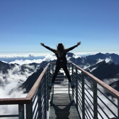 A woman stands on a viewing platform in Vysoké Tatry, Slovakia, surrounded by clouds and mountains, embracing freedom.