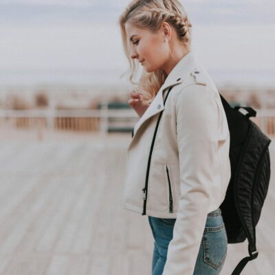 A young woman in a leather jacket walking on a boardwalk, embracing a casual and stylish vibe.