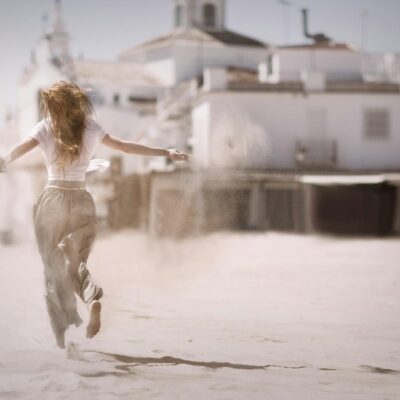 Back view of a young woman jumping and enjoying on a sunny beach, embodying freedom and happiness.