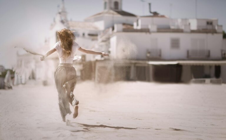 Back view of a young woman jumping and enjoying on a sunny beach, embodying freedom and happiness.